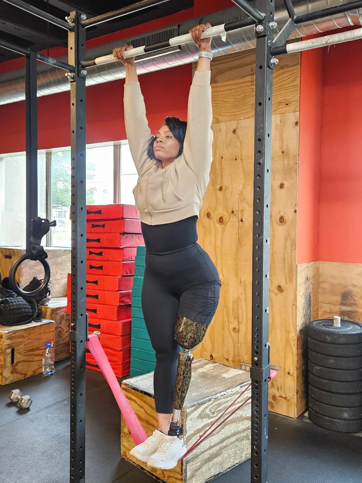 Kalisha hanging from a pull-up bar at the gym, with her prosthetic leg visible